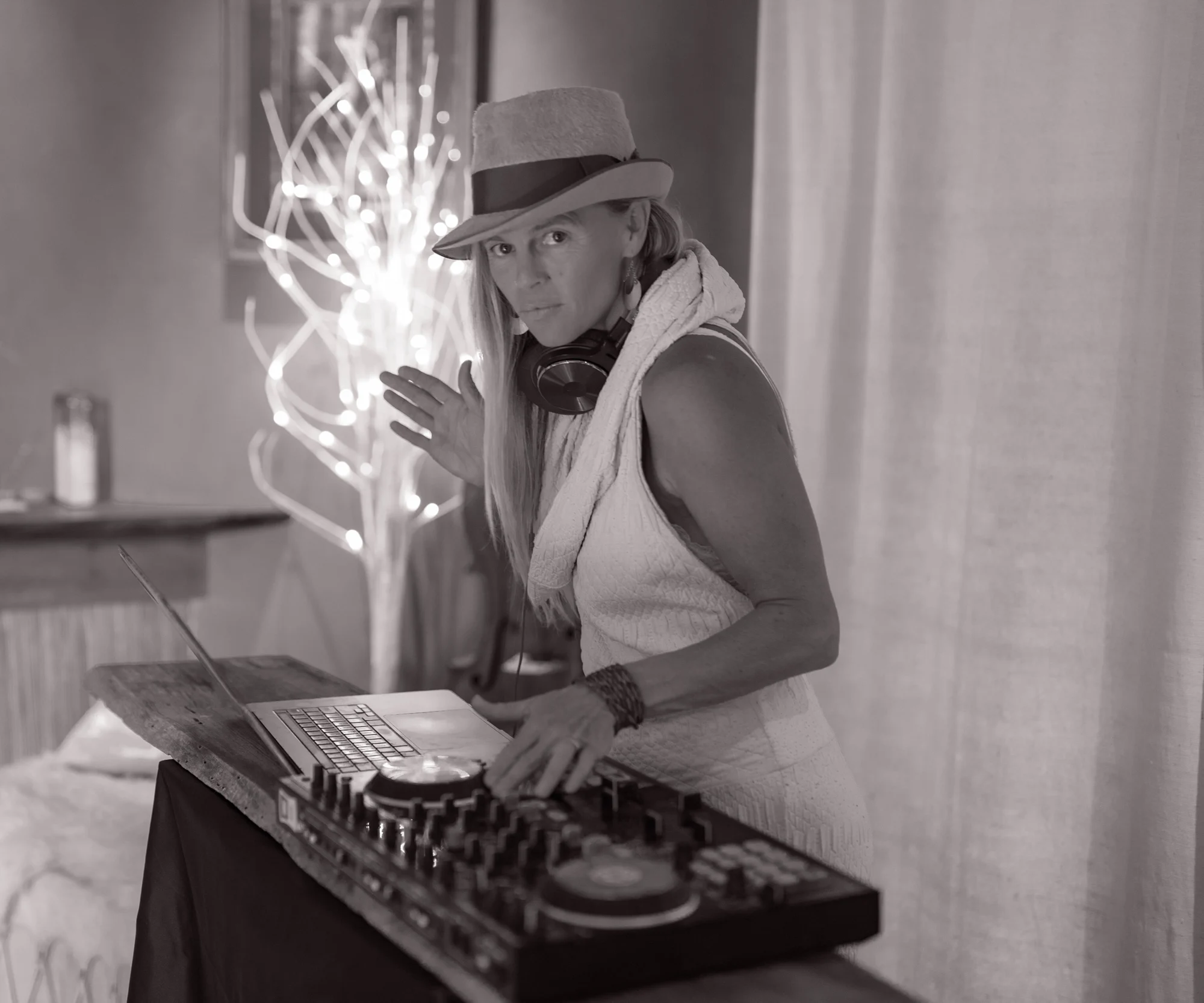 Asha in a hat and headphones behind the decks, photographed in black and white