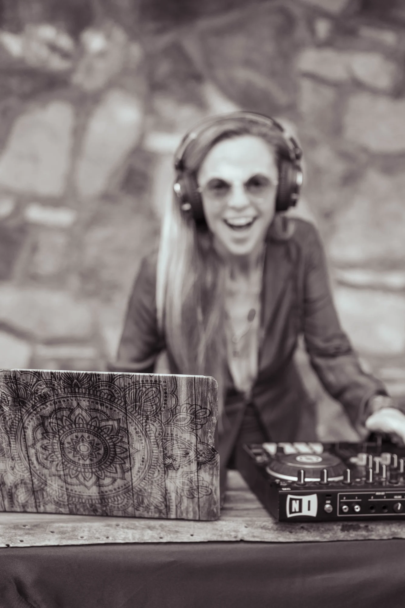 Asha smiling in headphones at her DJ setup, in black and white