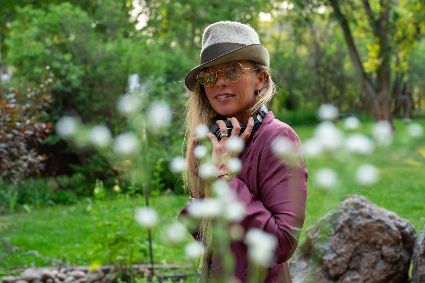 Asha in her plum suit and hat, holding her headphones among soft white flowers